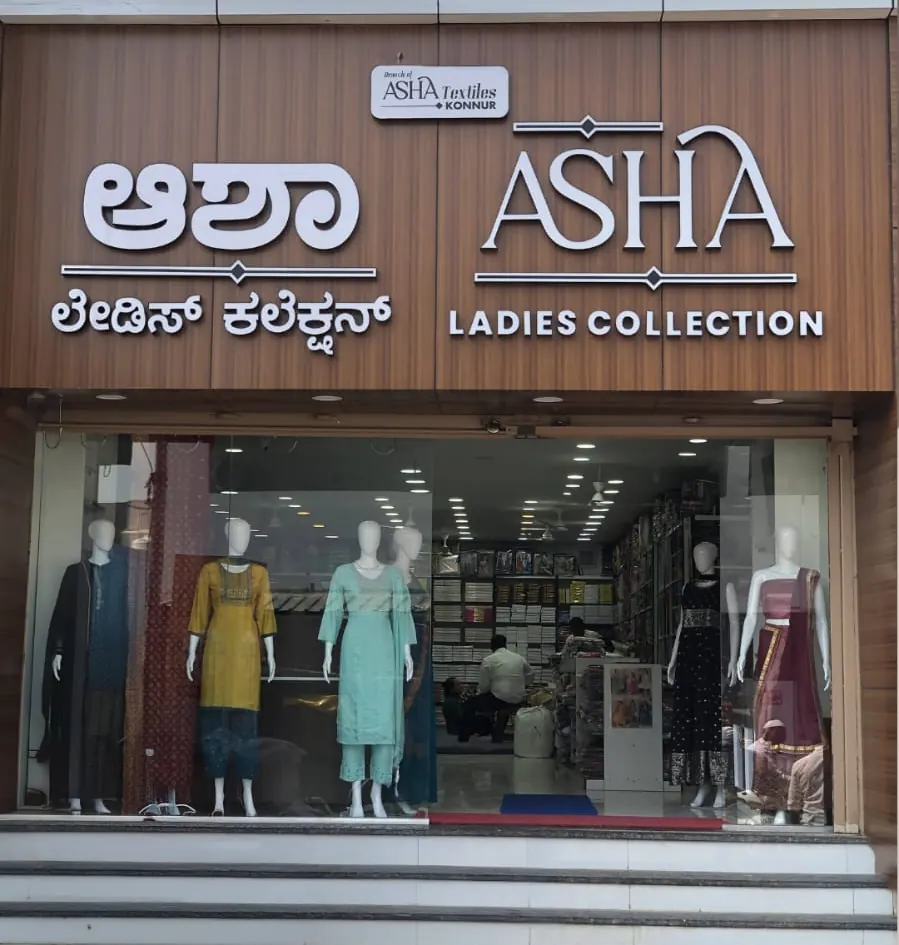 The ASHA Ladies Collection shop front in daylight, with the Kannada and English signboards and dressed mannequins in the windows